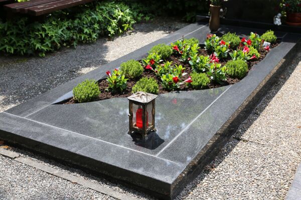Foto: Ein Grab mit blühenden Pflanzen und einem Grablicht